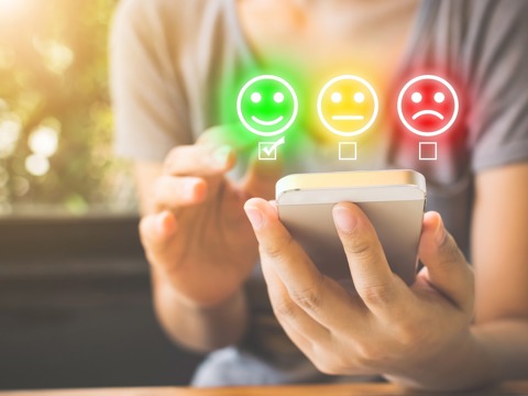A person uses a mobile phone to submit feedback. They have three options to choose from - happy, neutral and sad - indicated by graphics of facial expressions.