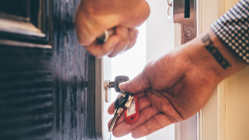 Close-up of a person unlocking a front door with a key, holding a set of keys in their hand.